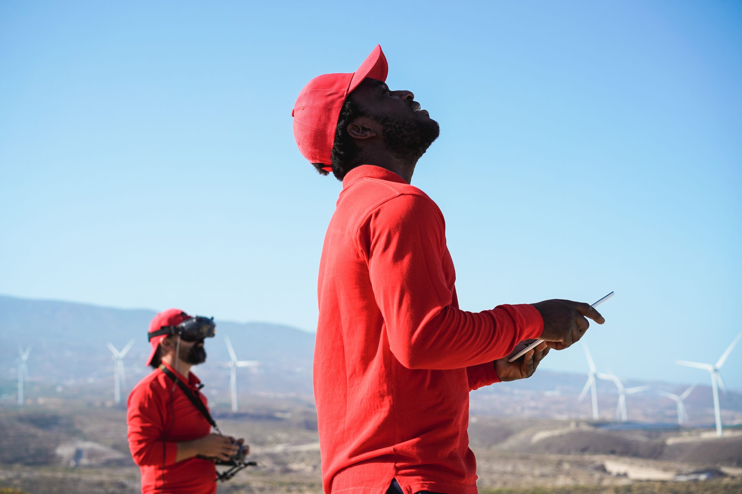 Multiracial engineer men using virtual reality headset on a windmill farm – Focus on african man hand holding digital tablet